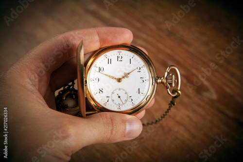 man's hand holds a vintage gold pocket watch on a wooden background