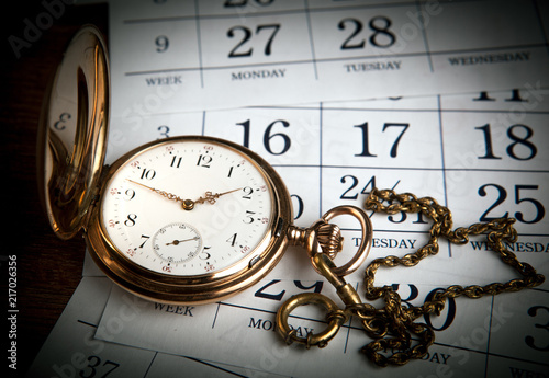 An antique gold pocket watch lies on calendar sheets photo