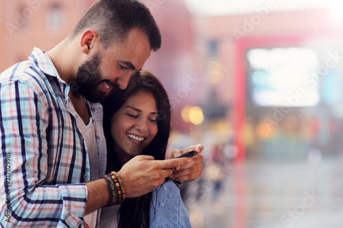 Happy couple using smartphone in city in rainy day