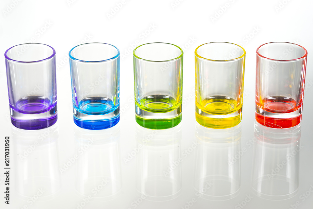 Five multicolored empty shot glasses placed symmetrically on a white background Five multicolored empty shot glasses placed symmetrically on a white background