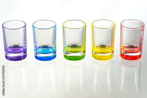 Five multicolored empty shot glasses placed symmetrically on a white background