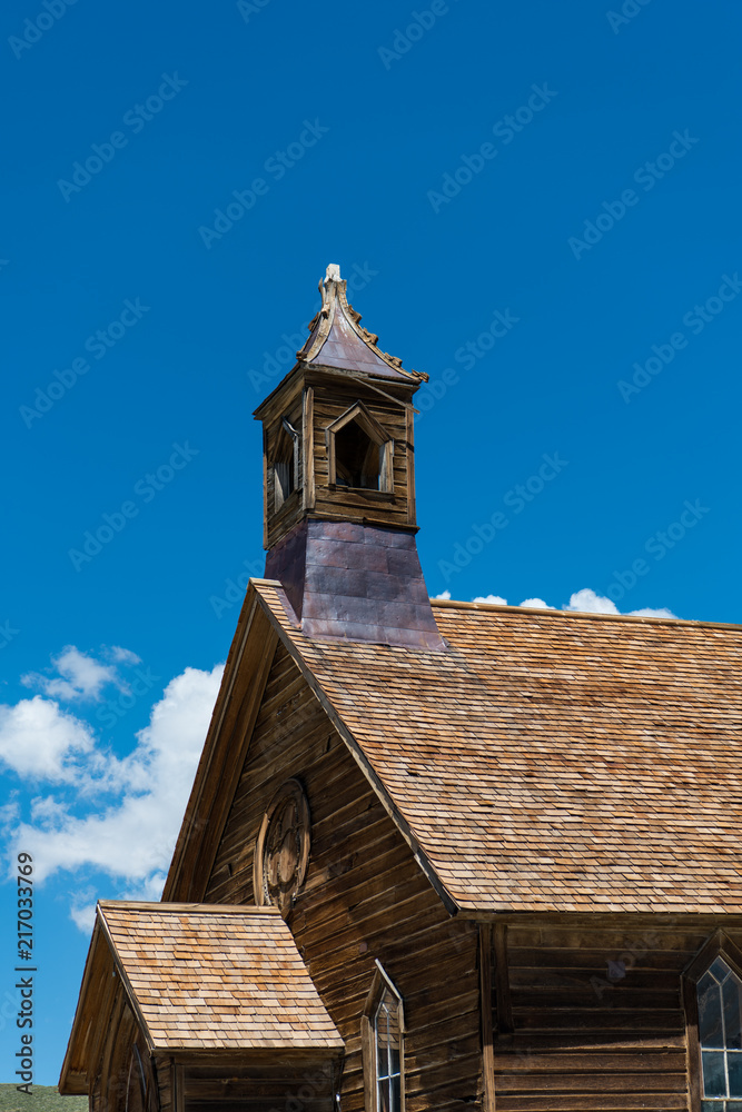 Abandoned old wooden church and steeple under beautiful blue sky and puffy clouds in the ghost town of Bodie, California