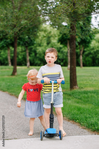 Two little Caucasian preschool children fighting in park outside. Boy and girl can not share one scooter. Older sibling brother not giving his toy to younger sister. Communication problems.