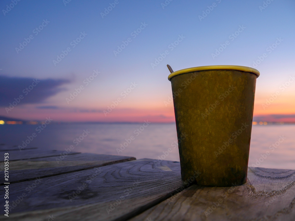 Paper tea or coffee cup, sunset sea background, early dark morning, coffee on sunrise or on sunset