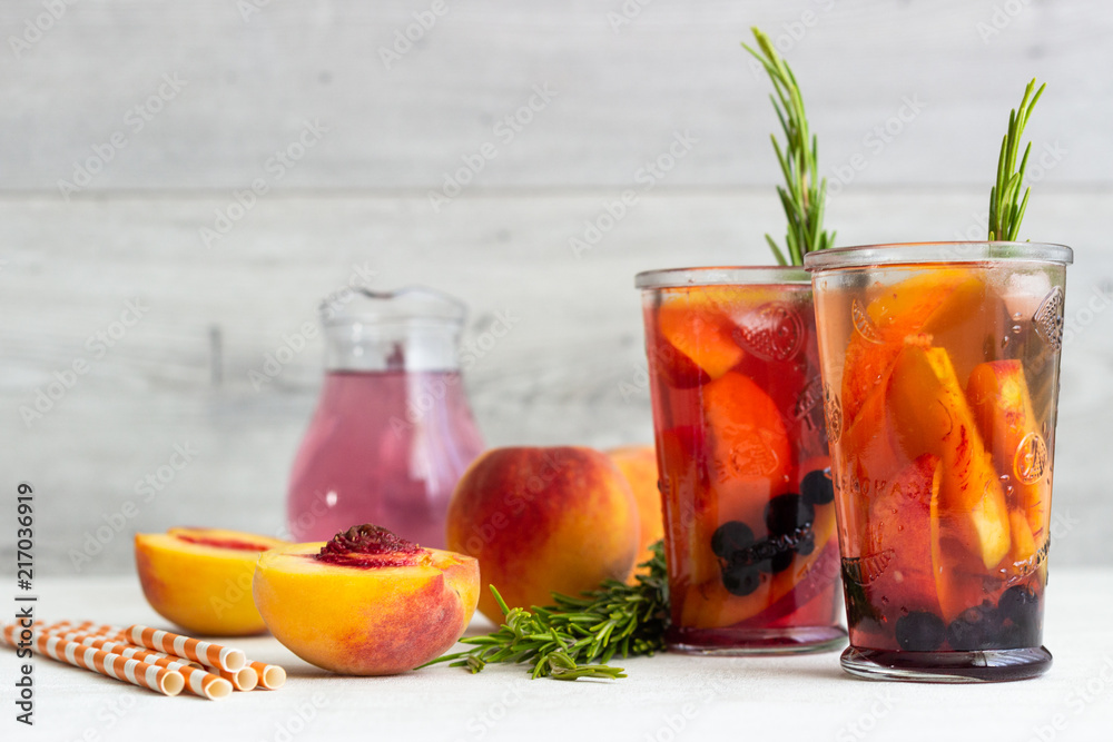 Peach and rosemary lemonade or cocktail in glass with fresh peaches on a light gray background. Summer cold drink. Peach and rosemary lemonade or cocktail in glass with fresh peaches on a light gray background. Summer cold drink.