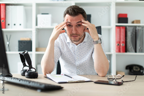 A young man sits at a table in the office and holds his hands behind his head. photo