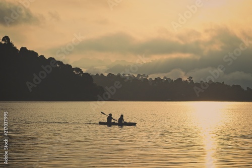 Two unrecognizable people canoeing on the Khao Sok lake in Thailand just before sunset. 