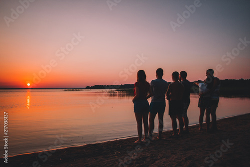 Silhouette of friends at the beach looking on the sunset in the summer evening