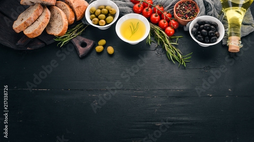 A set of olives, olive oil, bread, cheese and spices. On a black wooden background. Free space for text. © Yaruniv-Studio