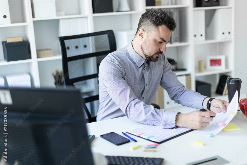 A young man in the office sits at a table, holds a marker in his hand and works with documents. A young man in the office sits at a table, holds a marker in his hand and works with documents.