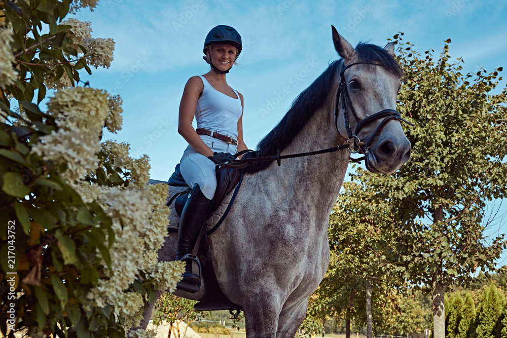 Obraz premium Female jockey on dapple gray horse walking through the flowering garden.