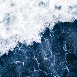The blue surf of the sea with white waves,  splash,  foam and bubbles at high tide and surf, aqua abstract background