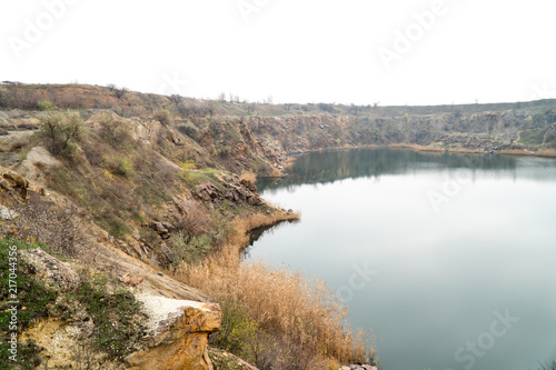 A water-filled quarry with a rocky shore. Sprouted reeds in different places