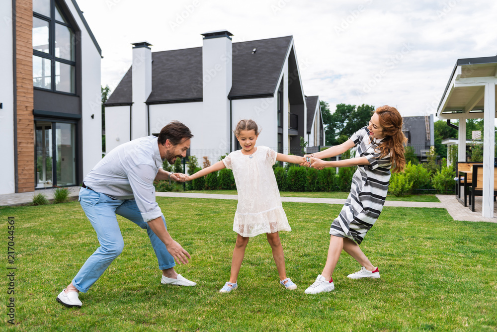 Obraz premium Young daughter. Pleasant cute girl standing between her parents while spending time with her family