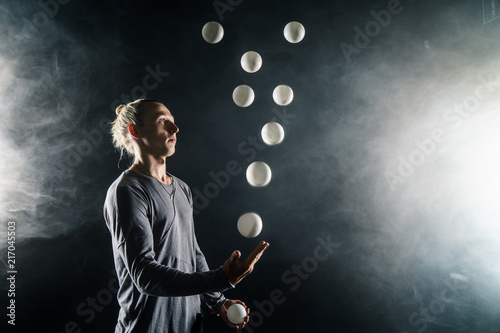 Blond juggler with white balls on black background