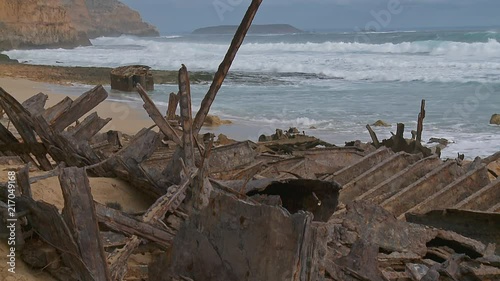 Wide shot of a beach covered in a ship wreck's rust debris with steep cliffs and rough surf in the background photo