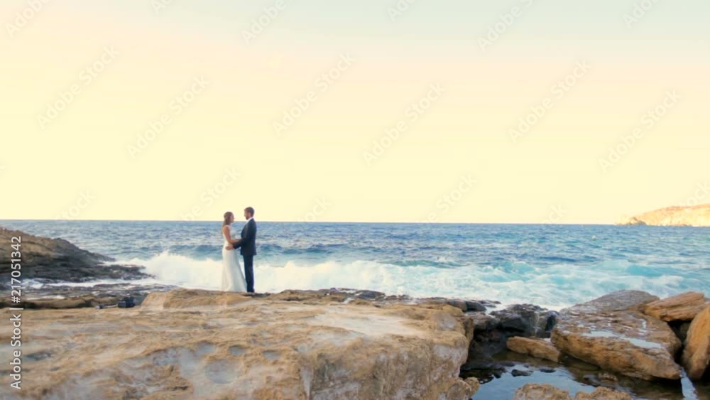Happy bride and groom tenderly embrace on the stone shore of the sea on a sunny day. Greece Happy bride and groom tenderly embrace on the stone shore of the sea on a sunny day. Greece