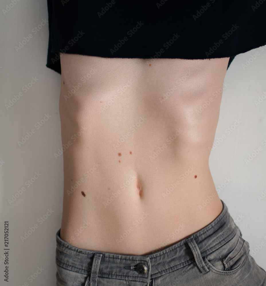 flat belly girl dressed in jeans lying on the floor on a white background.  T-shirt tucked up to her chest. Stock Photo