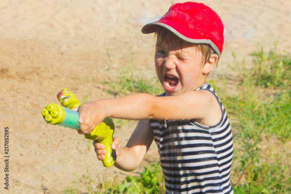 Child with a water pistol. The boy shoots water from a water pistol. Stock Photo Adobe Stock