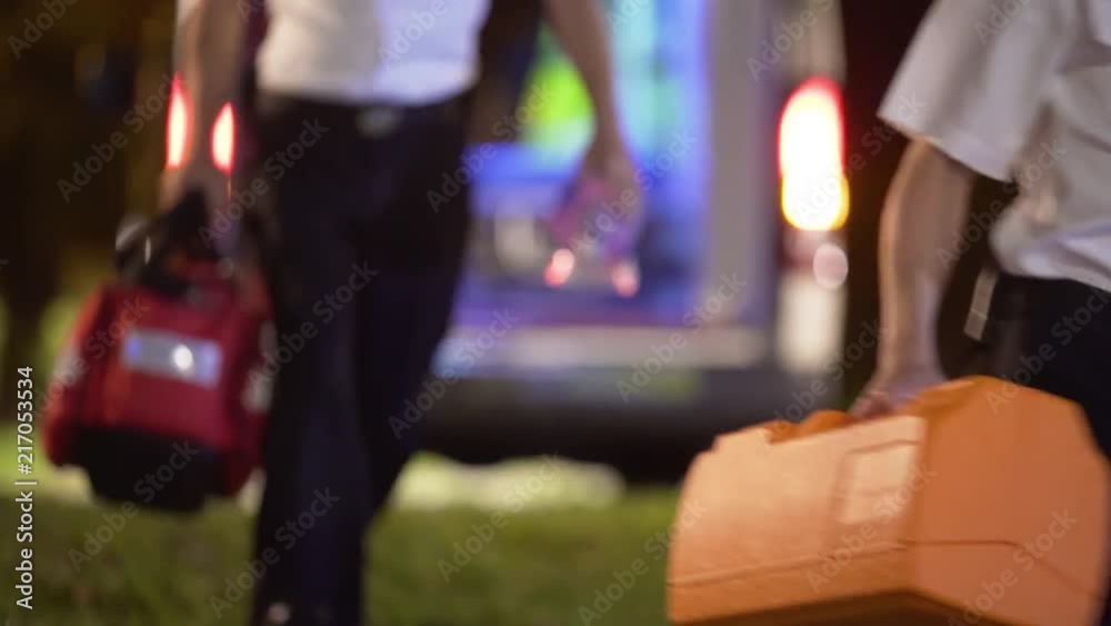 Paramedics run from an ambulance toward the camera and come into focus as they leave the frame. Medical emergency, first responder concept. Slow motion, focus blur.