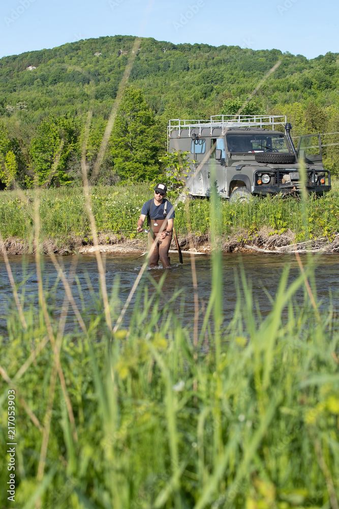 Fototapeta premium A man casts a fly in front of his Land Rover.