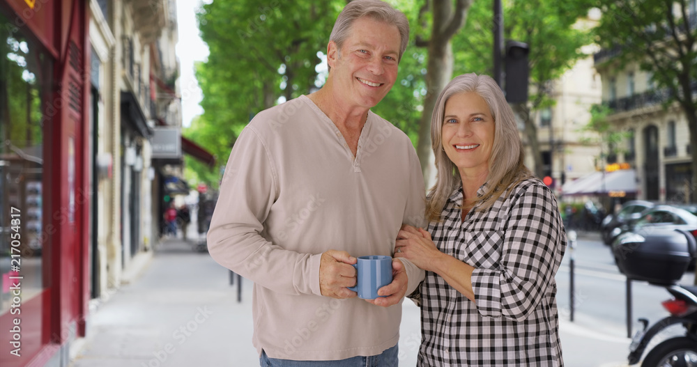 Loving old white couple stands happily on a Paris sidewalk