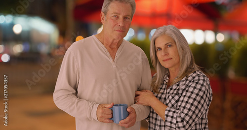 Mature Caucasian wife and husband on sidewalk looking seriously at camera