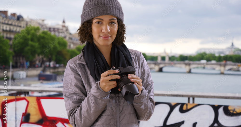 Portrait of cute millennial black female holding camera at Pont des Arts bridge in Paris
