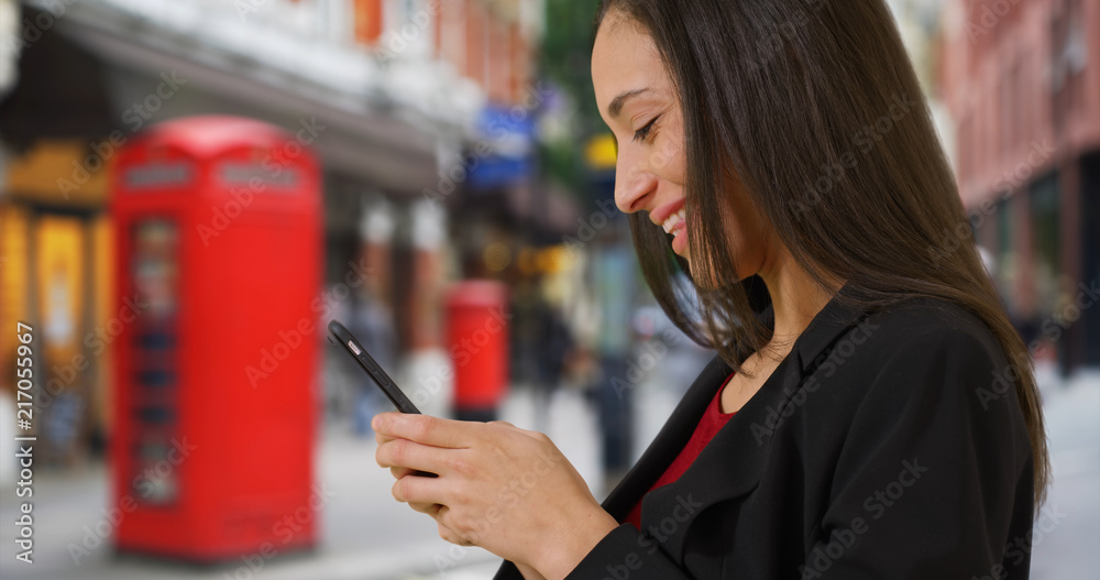 Side view of happy Latina female texting on cellphone on London street