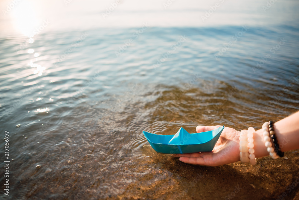 Girl holds a blue paper boat in the hands on a blue sea background. Summer by the sea Girl holds a blue paper boat in the hands on a blue sea background. Summer by the sea