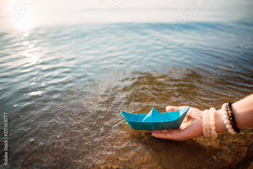Girl holds a blue paper boat in the hands on a blue sea background. Summer by the sea
