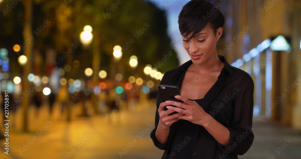 Millennial black woman tourist checks emails on phone at the Champs-Elysees Millennial black woman tourist checks emails on phone at the Champs-Elysees