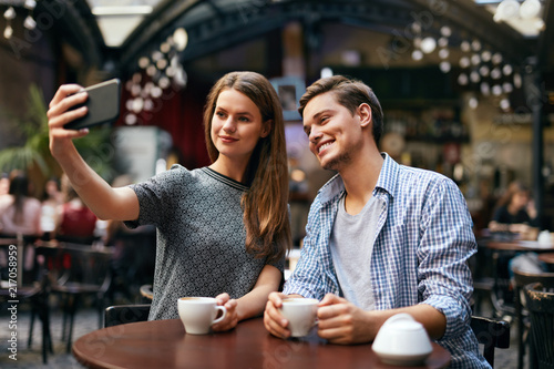 Couple Making Photo On Mobile Phone In Cafe