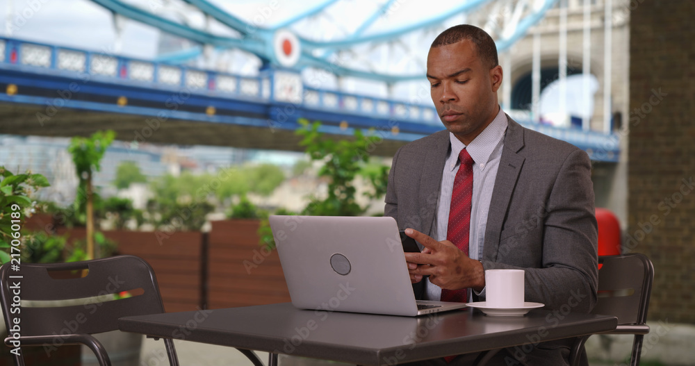 African corporate worker on his laptop sitting outside at a cafe in London