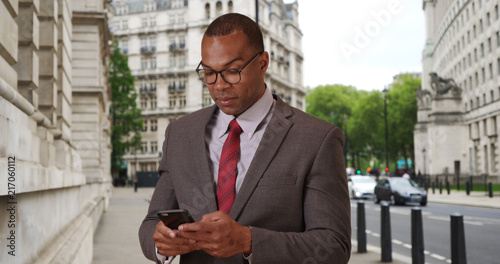 Modern African-American businessman in London sending texts with phone 