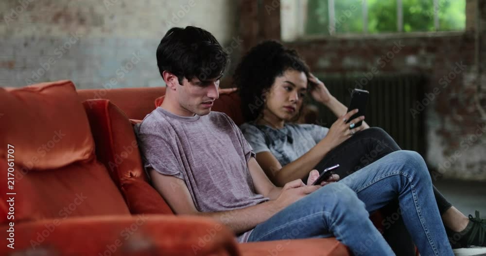 Millennials using smartphones relaxing on sofa Millennials using smartphones relaxing on sofa