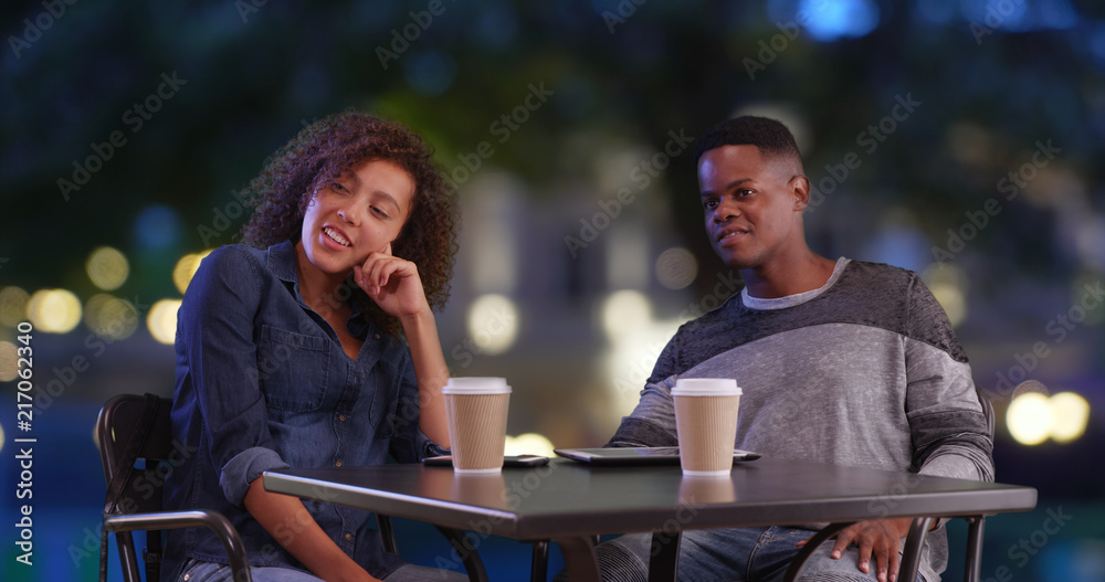 Black male and female enjoy evening outdoors drinking coffee and talking