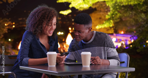 Black male and female meeting for coffee at night use tablet computer