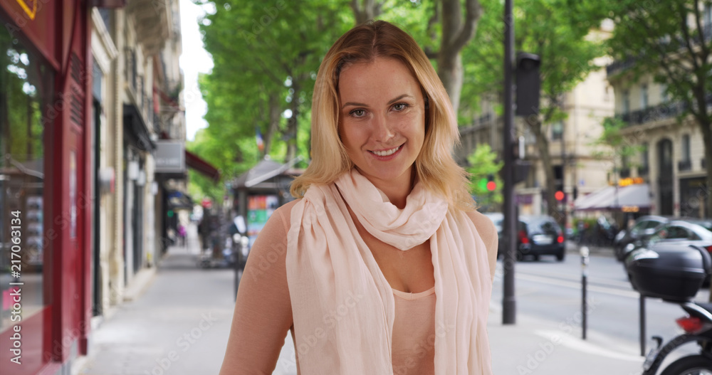 Elegant blonde white woman looking happily at camera outside on city sidewalk