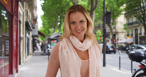 Elegant blonde white woman looking happily at camera outside on city sidewalk