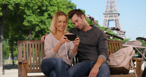 Cheerful young couple in Paris watching funny videos on smartphone