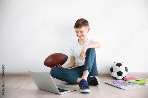 Cute little blogger with laptop and ball sitting on floor against light wall