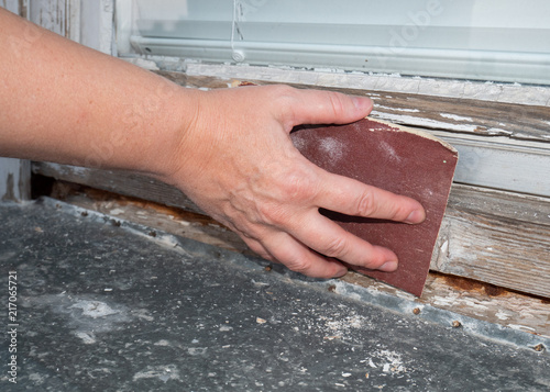hand sanding old coat of paint from a wooden window