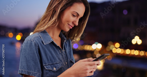 Smiling Caucasian woman using mobile phone outdoors at night