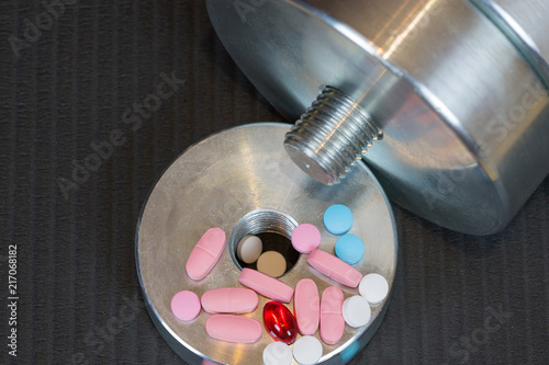 Dumbbell and vitamins pills on the gym mat