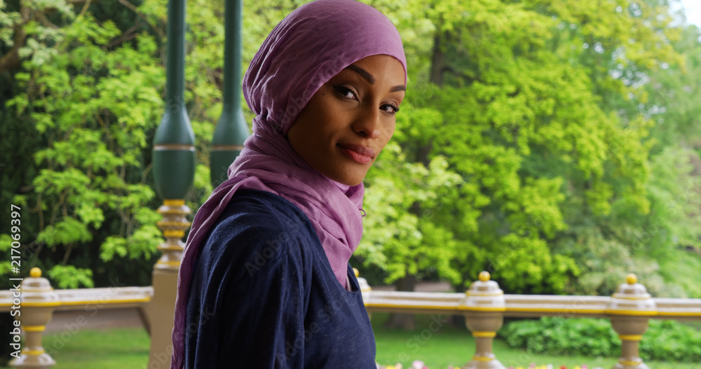 Naklejka premium Young Muslim woman using phone turns to smile at camera