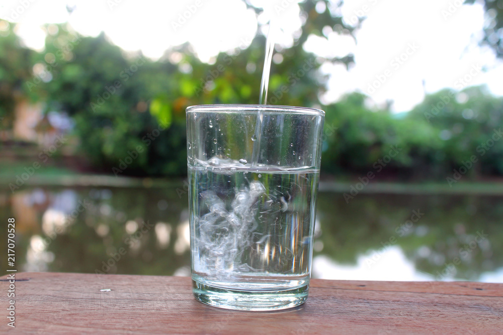 Close up pouring purified fresh drink water from the bottle on wooden table with nature background Close up pouring purified fresh drink water from the bottle on wooden table with nature background