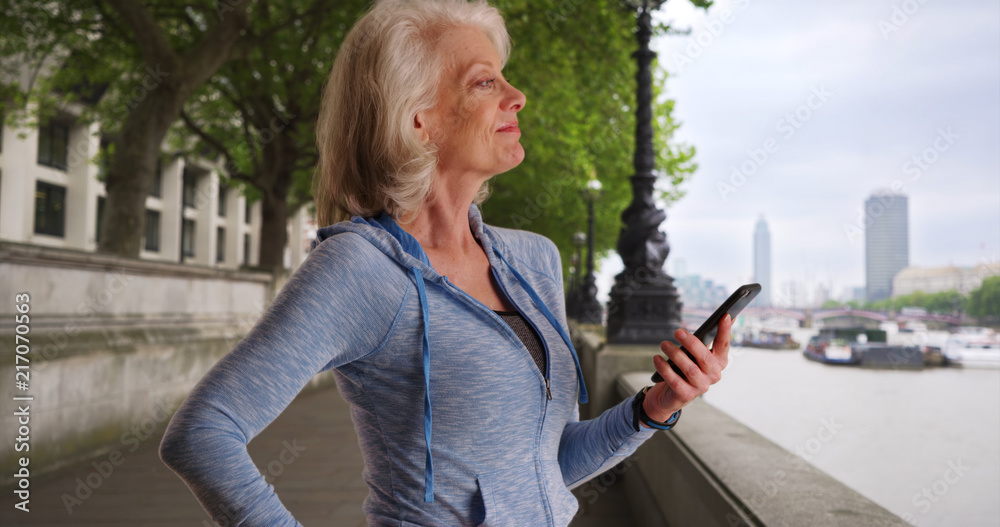 Fototapeta premium Active senior woman standing by river Thames in London texting on mobile phone
