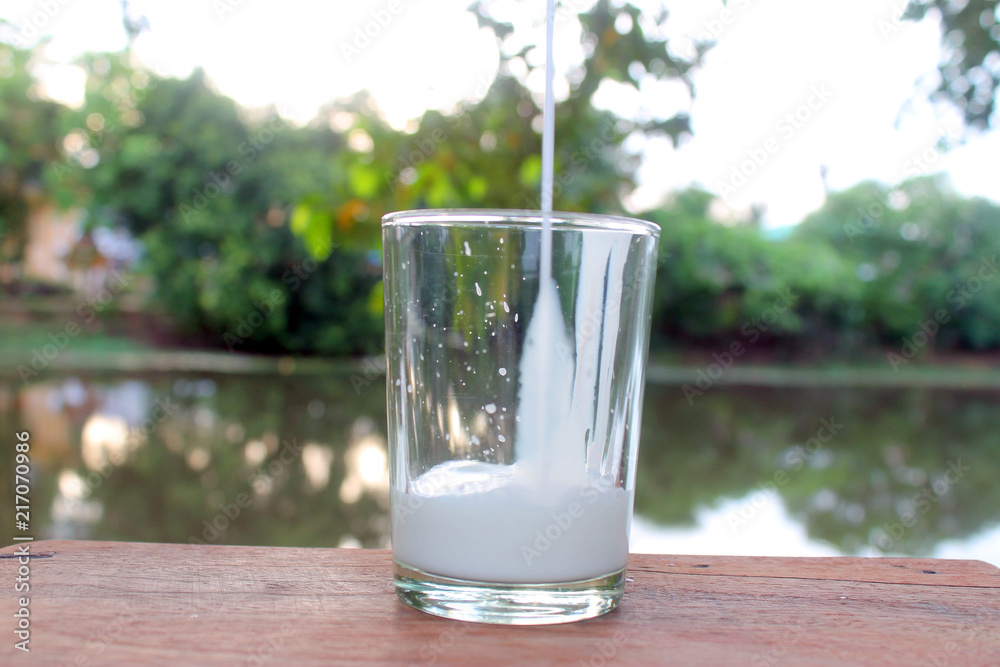 Close up pouring fresh milk from the bottle on wooden table with nature background Close up pouring fresh milk from the bottle on wooden table with nature background