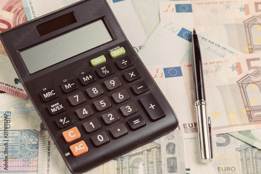 Black pen on pile of Euro banknotes with calculator, Business banking, accounting, personal finance or investment concept Black pen on pile of Euro banknotes with calculator, Business banking, accounting, personal finance or investment concept